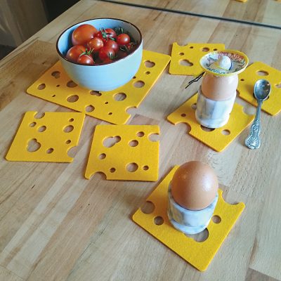 Zdjęcie przedstawia stół zastawiony śniadaniem. Pod jajkami znajdują się serwetki filcowe w kształcie plastrów sera w kolorze żółtym.
